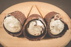 three ice cream with cone in chocolate/three ice cream with cone in chocolate on a round wooden support, selective focus stock photo three ice cream with cone in chocolate/three ice cream with cone in chocolate on a round wooden support, selective focus stock photo
