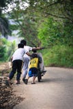 Three kids pushing motorbike on village road sloping slight uphill royalty free stock photography Three kids pushing motorbike on village road sloping slight uphill royalty free stock photography