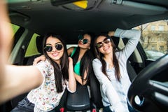 Three young cheerful women making selfie and smiling while sitting in car together