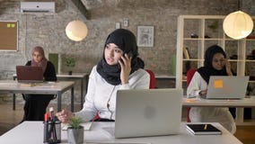 Three young muslim womens in hijab sitting and typing on laptop in modern office, beautiful muslim woman talking on stock video footage Three young muslim womens in hijab sitting and typing on laptop in modern office, beautiful muslim woman talking on stock video footage