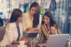 Three young women having conversation in cafe using lap top and stock photos Three young women having conversation in cafe using lap top and stock photos