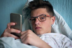 Tiener die in bed liggen en smartphone gebruiken Stock Foto's Tiener die in bed liggen en smartphone gebruiken Stock Foto's