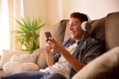Tiener die een mobiele telefoon met hoofdtelefoons het zitten met behulp van stock foto Tiener die een mobiele telefoon met hoofdtelefoons het zitten met behulp van stock foto