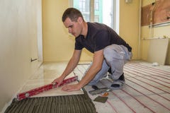 Tiler молодого работника устанавливая керамические плитки используя рычаг на пол цемента с системой провода электрического кабеля стоковые изображения Tiler молодого работника устанавливая керамические плитки используя рычаг на пол цемента с системой провода электрического кабеля стоковые изображения