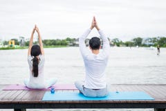 Tillbaka av mannen och den ?vande yoga och meditationen f?r kvinna p? mattt n?ra lagun band f?r m?tt f?r ?pplebegreppsh?lsa royaltyfria foton Tillbaka av mannen och den ?vande yoga och meditationen f?r kvinna p? mattt n?ra lagun band f?r m?tt f?r ?pplebegreppsh?lsa royaltyfria foton