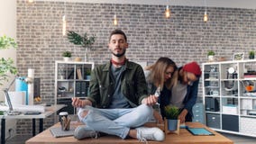 Time-lapse of handsome young man relaxing in lotus position on desk in office stock video footage Time-lapse of handsome young man relaxing in lotus position on desk in office stock video footage