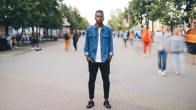 Time-schackningsperiod stående av den deprimerade afrikansk amerikanmannen som ser kameran som bara står i gatan, händer i fack arkivfilmer Time-schackningsperiod stående av den deprimerade afrikansk amerikanmannen som ser kameran som bara står i gatan, händer i fack arkivfilmer
