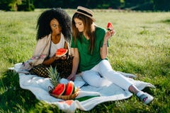 Timespending de duas namoradas multi-étnicas A menina consideravelmente africana está conversando através do móbil e está comendo fotografia de stock royalty free Timespending de duas namoradas multi-étnicas A menina consideravelmente africana está conversando através do móbil e está comendo fotografia de stock royalty free