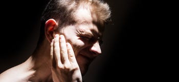Tinnitus, man on a black background isolated holding a sick ear, suffering from pain royalty free stock photography Tinnitus, man on a black background isolated holding a sick ear, suffering from pain royalty free stock photography