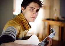 Tipo in chitarra acustica gialla dei giochi del maglione mentre sedendosi a casa immagini stock libere da diritti Tipo in chitarra acustica gialla dei giochi del maglione mentre sedendosi a casa immagini stock libere da diritti