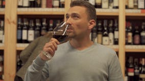 Tipo pensieroso bello con un vetro di vino in un negozio di alcolici La donna nei precedenti sta scegliendo una bottiglia di vino archivi video Tipo pensieroso bello con un vetro di vino in un negozio di alcolici La donna nei precedenti sta scegliendo una bottiglia di vino archivi video