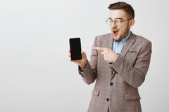 Tir de studio du type barbu drôle amusé avec plaisir dans les verres et la veste élégante tenant le smartphone se dirigeant au di images libres de droits Tir de studio du type barbu drôle amusé avec plaisir dans les verres et la veste élégante tenant le smartphone se dirigeant au di images libres de droits