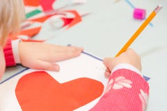 Tiraggio del bambino una cartolina I bambini sono impegnati in cucito La ragazza firma una cartolina il 14 febbraio immagine stock libera da diritti Tiraggio del bambino una cartolina I bambini sono impegnati in cucito La ragazza firma una cartolina il 14 febbraio immagine stock libera da diritti