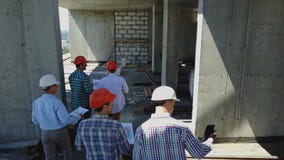 Tiro aéreo del grupo de Buiders que camina en el emplazamiento de la obra que lleva a cabo el plan del edificio de Experting de l almacen de video Tiro aéreo del grupo de Buiders que camina en el emplazamiento de la obra que lleva a cabo el plan del edificio de Experting de l almacen de video