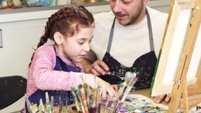 Tiro cosechado de hablar sonriente de la niña linda con sus pinturas de mezcla del papá en la clase de arte Tiro cosechado de hablar sonriente de la niña linda con sus pinturas de mezcla del papá en la clase de arte
