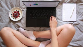 Tiro de arriba de los pies, del ordenador portátil, del yogur y del cuaderno de la mujer en la manta gris Tiro de arriba de los pies, del ordenador portátil, del yogur y del cuaderno de la mujer en la manta gris