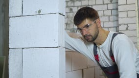 Tiro inclinable del constructor joven en pared de pulido del bloque del desgaste del trabajo con la herramienta abrasiva metrajes Tiro inclinable del constructor joven en pared de pulido del bloque del desgaste del trabajo con la herramienta abrasiva metrajes