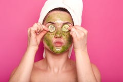 Tiro interno da mulher atrativa nova com máscara verde em sua cara que põe as partes do pepino sobre seus olhos, projetando-se se imagem de stock royalty free Tiro interno da mulher atrativa nova com máscara verde em sua cara que põe as partes do pepino sobre seus olhos, projetando-se se imagem de stock royalty free