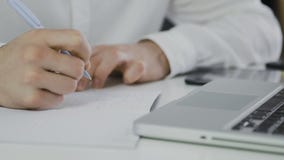 Tiro macro do homem de negócios que usa o laptop e redigindo para baixo a informação em seu bloco de notas vídeos de arquivo Tiro macro do homem de negócios que usa o laptop e redigindo para baixo a informação em seu bloco de notas vídeos de arquivo