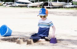 Toddler with Hat & Sunglasses Plays on a Sandy Beach Building Sand Castles stock photography Toddler with Hat & Sunglasses Plays on a Sandy Beach Building Sand Castles stock photography