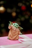 TOKYO, JAPAN - DECEMBER 04, 2020 - Star Wars Figures Baby Yoda stands on a pink gift box. Blurred background. Christmas Tree