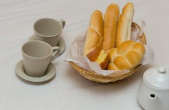 Tomam o café da manhã dois copos um bule com uma cesta do pão fresco com os anéis de espuma franceses dos baguettes fotografia de stock royalty free Tomam o café da manhã dois copos um bule com uma cesta do pão fresco com os anéis de espuma franceses dos baguettes fotografia de stock royalty free