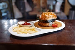 Tomate, patatas fritas y salsa de tomate adornados hamburguesa en una placa oval en una tabla de madera imagen de archivo Tomate, patatas fritas y salsa de tomate adornados hamburguesa en una placa oval en una tabla de madera imagen de archivo