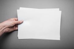 Tomt horisontalark A4 på en grå bakgrund i en manlig europeisk hand som är falsk upp arkivfoto Tomt horisontalark A4 på en grå bakgrund i en manlig europeisk hand som är falsk upp arkivfoto