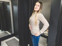 Toned portrait of beautiful smiling young woman trying on sweater in fitting room and looking in the big mirror royalty free stock image Toned portrait of beautiful smiling young woman trying on sweater in fitting room and looking in the big mirror royalty free stock image