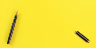 Top down view - black fountain ink pen with gold nib, opened, cap on the right, yellow background, space for text royalty free stock images Top down view - black fountain ink pen with gold nib, opened, cap on the right, yellow background, space for text royalty free stock images