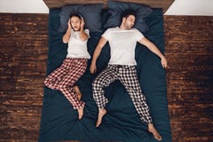 Top view. Annoyed woman in headphones tries not to hear snoring of adult young man. stock photo Top view. Annoyed woman in headphones tries not to hear snoring of adult young man. stock photo