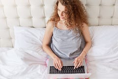 Top view of beautiful woman with curly hair looks positively aside, works freelance at home, keyboards on laptop computer, creats royalty free stock images Top view of beautiful woman with curly hair looks positively aside, works freelance at home, keyboards on laptop computer, creats royalty free stock images
