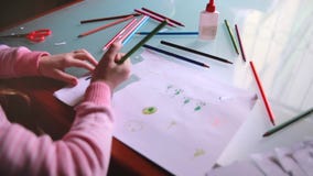 Top view camera sliding left on little Caucasian girl child drawing on paper with various color pencils at a table. stock video Top view camera sliding left on little Caucasian girl child drawing on paper with various color pencils at a table. stock video
