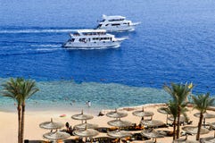 Top view of a sandy beach with sunbeds and sun umbrellas and two large white ships, a boat, a cruise liner floating in the sea on stock image Top view of a sandy beach with sunbeds and sun umbrellas and two large white ships, a boat, a cruise liner floating in the sea on stock image