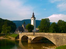 Torre di chiesa e ponte della pietra nel lago Bohinj immagini stock Torre di chiesa e ponte della pietra nel lago Bohinj immagini stock