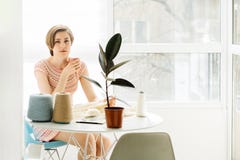 Toughtful craftswoman relaxing with coffee cup whole knitting dress with crochet in cozy workplace at home interior. Female stock photo Toughtful craftswoman relaxing with coffee cup whole knitting dress with crochet in cozy workplace at home interior. Female stock photo