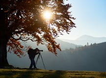 Touristischer Mann des Wanderers mit Kamera auf grasartigem Tal auf Hintergrund von Berglandschaft unter großem Baum lizenzfreies stockfoto Touristischer Mann des Wanderers mit Kamera auf grasartigem Tal auf Hintergrund von Berglandschaft unter großem Baum lizenzfreies stockfoto