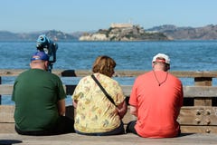 Tourists sitting on a bench with views of the island and Alcatraz prison in the background from Pier 39 in San Francisco stock images Tourists sitting on a bench with views of the island and Alcatraz prison in the background from Pier 39 in San Francisco stock images