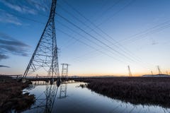 Tours électriques avec de principales lignes au coucher du soleil, avec des réflexions dans l'eau photos stock Tours électriques avec de principales lignes au coucher du soleil, avec des réflexions dans l'eau photos stock