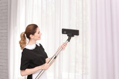 Trabajador de sexo femenino que quita el polvo de las cortinas con el aspirador profesional, dentro imagenes de archivo Trabajador de sexo femenino que quita el polvo de las cortinas con el aspirador profesional, dentro imagenes de archivo