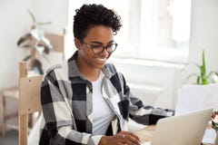 Trabajo femenino afroamericano sonriente con el ordenador portátil y los papeles foto de archivo Trabajo femenino afroamericano sonriente con el ordenador portátil y los papeles foto de archivo