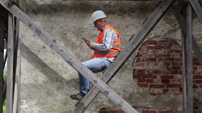 Trabalhador da construção que senta-se no andaime de madeira e que usa o PC da tabuleta filme Trabalhador da construção que senta-se no andaime de madeira e que usa o PC da tabuleta filme