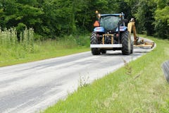 Tracteur fauchant l'herbe du côté d'une route de campagne image libre de droits Tracteur fauchant l'herbe du côté d'une route de campagne image libre de droits