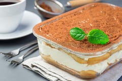 Traditional italian Tiramisu dessert cake in a glass form, decorated with cocoa powder and mint, with coffee cup, on a gray stock images Traditional italian Tiramisu dessert cake in a glass form, decorated with cocoa powder and mint, with coffee cup, on a gray stock images