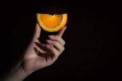 Tranche orange dans des doigts femelles sur le fond noir image stock Tranche orange dans des doigts femelles sur le fond noir image stock