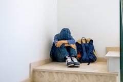 Trauriger Junge mit dem Rucksack, der allein in der Ecke im Treppenhaus sitzt stockfoto Trauriger Junge mit dem Rucksack, der allein in der Ecke im Treppenhaus sitzt stockfoto