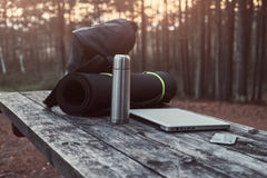 Travel Concept. Backpack, Tourist Mat, Laptop, Smartphone And Thermos Bottle On A Wooden Table In Beautiful Forest. Royalty Free Stock Photo