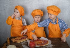 Tre ragazzi europei svegli vestiti come cuochi sono occupati cucinare la pizza i tre fratelli aiutano mia madre a cucinare la piz fotografia stock Tre ragazzi europei svegli vestiti come cuochi sono occupati cucinare la pizza i tre fratelli aiutano mia madre a cucinare la piz fotografia stock