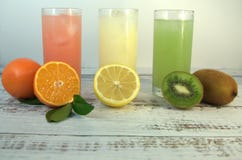 Tre vetri di vetro con un succo e un ghiaccio di rinfresco, su una metà affettata del supporto del tessuto intera e, di un'aranci immagine stock Tre vetri di vetro con un succo e un ghiaccio di rinfresco, su una metà affettata del supporto del tessuto intera e, di un'aranci immagine stock