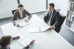 Trois gens d'affaires s'asseyant autour d'une table et ayant une réunion d'affaires, vue courbe photographie stock libre de droits Trois gens d'affaires s'asseyant autour d'une table et ayant une réunion d'affaires, vue courbe photographie stock libre de droits